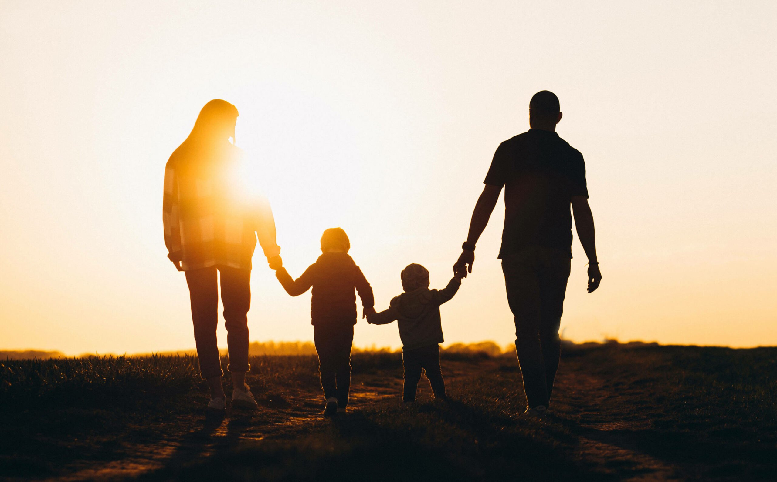 A family of four, holding hands walking in the sunset.